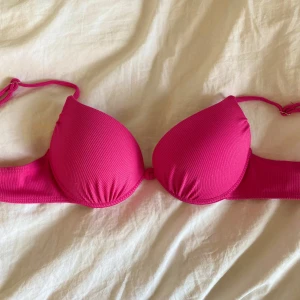 Rosa bikiniöverdel med vadderade kupor - Säljer en rosa bikiniöverdel med vadderade kupor och knyt i ryggen. Bikinin har en ribbad struktur och är tillverkad i polyester och elastan. Perfekt för sommardagar vid stranden eller poolen.