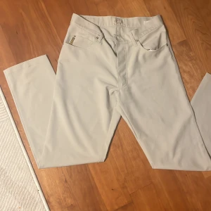 Beige jeansbyxor från Armani Jeans - Snygga beige jeansbyxor från Armani Jeans med klassisk femficksdesign och silverfärgad logga på bakfickan. Byxorna har raka ben och normal passform, perfekt för en stilren look. Märkespatch i läder bak i midjan.