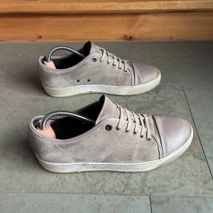 Beige sneakers från Lanvin - Säljer ett par stilrena beige sneakers från Lanvin med rund tå och platt sula. Skorna har snörning och är tillverkade i mocka med detaljer i skinn. Perfekta för en clean och avslappnad look. Skorna är andvönda och är i 6/10 skick pris kan diskuteras 