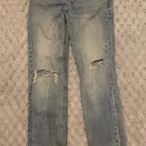 Ljusblå slitna jeans från Zara - Ljusblå jeans från Zara med raka ben och slitna detaljer på båda knäna. Klassisk femficksmodell med dragkedja och knapp. Perfekta för en avslappnad och trendig look.