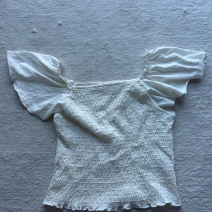 Vit smockad topp med puffärmar från Kappahl - Säljer en söt vit smocked topp från Kappahl. Den är volanger på ärmarna och lite nedtill. Storleken är 158/164