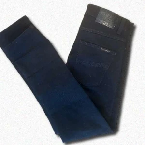 Svarta jeansbyxor från Nudie Jeans - Säljer ett par Nudie Jeans i modellen Grim Tim, storlek 30/30. Färgen är “Dry Everblack” – en riktigt djup svart denim som är designad för att behålla färgen längre än vanliga svarta jeans. Klassisk slim fit med rak passform från knäna och ner. Material: 98 % bomull, 2 % elastan – bekväma med lite stretch. I fint skick, sparsamt använda och utan skador.  Nypris ca 1500 kr. Mitt pris: 500