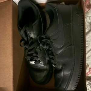 Svarta Nike Air Force 1 sneakers - Säljer ett par klassiska helsvarta Nike Air Force 1 sneakers. Skorna har en låg profil, rund tå och snörning framtill. Perfekta för dig som gillar en stilren och tidlös look. Passar till det mesta och är riktigt bekväma. 