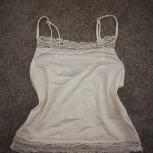 Vit spetsdetaljerad linnetopp - Säljer en söt vit linnetopp från H&M med tunna axelband, som går att justera, och spetsdetaljer upptill och nedtill. Använd någon enstaka gång 