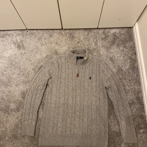 Ralph Lauren half zip - Säljer en klassisk grå kabelstickad tröja från Polo Ralph Lauren med halv dragkedja och broderad logga på bröstet. Taggar finns med. Skriv om du har några funderingar🤗