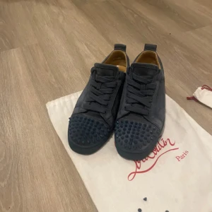 Mörkblå sneakers med nitar från Christian Louboutin - Säljer ett par mörkblå sneakers från Christian Louboutin med karakteristiska nitar på tån och klassisk röd sula. Skorna har snörning och är tillverkade i mocka. Perfekta för dig som vill sticka ut med exklusiv stil. Storlek 40 men passar 41 priset kan gå ner i snabb affär. Dem är legitcheckade av Cetire. Hör av er vid minsta lilla
