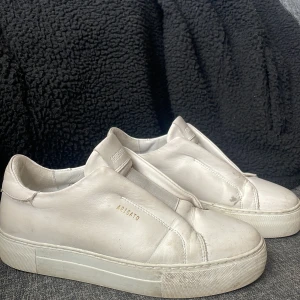 Arigato 360 laceless skor - Säljer ett par stilrena vita sneakers från Axel Arigato med minimalistisk design och diskret logga på sidan. Skorna har en tjock vit sula och är tillverkade i skinn. Perfekta för dig som gillar clean och enkel stil.