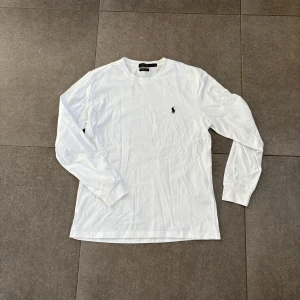 Vit långärmad Ralph Lauren tröja - Säljer en klassisk vit långärmad tröja från Polo Ralph Lauren med broderad logga på bröstet. Tröjan har rund halsringning och är i en slim fit-modell. Perfekt för en stilren och enkel look. Använd 1-2 gånger. 