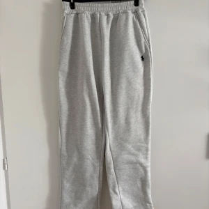 Grå mjukisbyxor från Polo Ralph Lauren - Snygga ljusgrå mjukisbyxor från Polo Ralph Lauren med elastisk midja och sidofickor. Byxorna har en liten svart broderad logga på ena benet och är tillverkade i mjuk bomull. Perfekta för en avslappnad stil. Passform: Baggy/loose