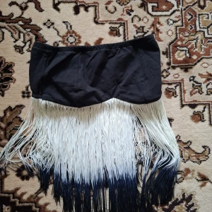 Svart och vit franskjol - Säljer en unik kjol med svart midjeband och långa vita fransar som övergår i svart nertill. Perfekt för dig som vill sticka ut med en cool och dansvänlig look.