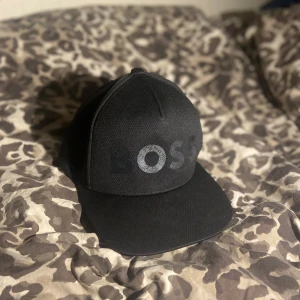 Boss keps  - Snygg svart keps från BOSS med stort BOSS-tryck framtill i grått med mönster. Säljer eftersom den inte passar min huvudform, annars skit snygg keps i näst intill ny-skick