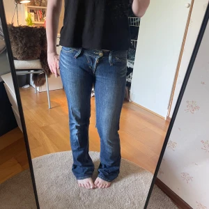Lågmidjade bootcut jeans från Lee - Säljer ett par klassiska blå jeans från Lee med bootcut passform. Jeansen har låg midja, dragkedja och knäppning framtill samt snygga detaljerade bakfickor med dragkedjor. Perfekta till vardags och lätta att matcha.