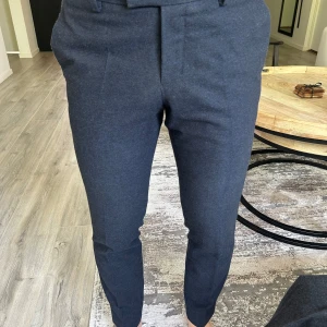 Mörkgrå kostymbyxor från Tiger of Sweden - Säljer ett par stilrena marinblå kostymbyxor från Tiger of Sweden. Byxorna har normal passform, pressveck och knäppning fram. Storlek: 48