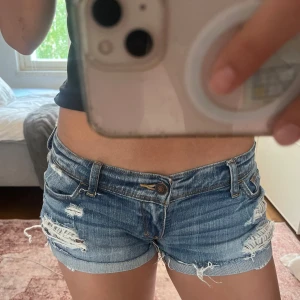 Blå jeansshorts från Abercrombie & Fitch - Säljer ett par blå jeansshorts från Abercrombie & Fitch med slitna detaljer. Modellen är lågmidjad. Storlek w25