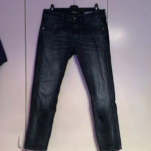 Replay Anbass jeans i mörkblå denim - Säljer ett par snygga Replay Anbass jeans i mörkblå tvätt med klassisk femficksdesign. Jeansen har normal passform, dragkedja och raka ben. Perfekta för dig som gillar stilrena och bekväma jeans med diskreta slitningar.