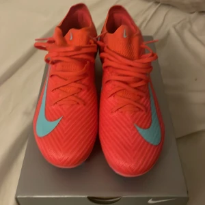 Säljer för jag behöver nya som passar för gräs, svara snabbt gärna! Priset kan också diskuteras. - Säljer ett par röda Nike fotbollsskor med turkos swoosh. Skorna har snörning och en modern, sportig design som sticker ut på planen. Perfekta för dig som vill ha både stil och funktion under matchen.
