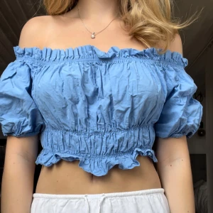 Sommartopp - Säljer en ljusblå offshoulder topp från Zara med puffärmar och smockdetaljer. Toppen är croppad och har volangkant både upptill och nertill. Superfin till sommaren!😍