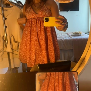 Röd/rosa paisleymönstrad kortklänning - Säljer en röd/rösa kortklänning med vitt paisleymönster och smala axelband. Klänningen har v-ringning och pärlstukatur på överdelen💓 Perfekt för varma dagar!