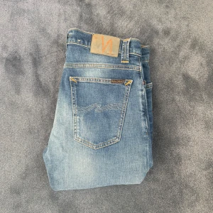 Blå jeans från Nudie Jeans - Säljer ett par snygga bla jeans från Nudie Jeans med klassisk femficksdesign och subtila slitningar. Jeansen har en straight passform och är tillverkade i högkvalitativt denim. Perfekta för en avslappnad stil. Längd 104cm midja 40,5cm