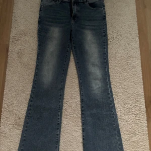 Blå bootcut jeans med broderade bakfickor - Säljer ett par blå bootcut jeans med snygga broderade detaljer och knappar på bakfickorna. Jeansen har en klassisk tvätt och normal passform, perfekta till vardags. Fickor både fram och bak. Passat för storlek XL då de är stretchiga i midjan 