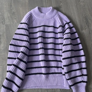 Lila stickad tröja med svarta ränder - Säljer en lila stickad tröja med svarta horisontella ränder. Tröjan har rund halsringning, långa ärmar och en avslappnad passform. Använd endast en eller två gånger!