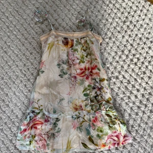 Blommig sommarklänning med volang - Söt blommig klänning med tunna axelband och volangdetalj nertill. Klänningen har en ljus bas med färgglada blommor i rosa, grönt och gult. Perfekt för varma dagar och har en luftig känsla.