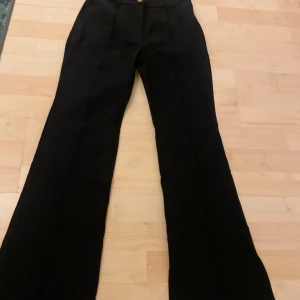 Svarta kostymbyxor från SHEIN - Säljer ett par svarta kostymbyxor från SHEIN i modellen Petite XXS. Byxorna har hög midja, vida ben och stängs med knapp och dragkedja. Perfekta för en stilren och klassisk look.