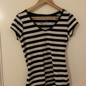 Svartvit randig t-shirt från Basics - Säljer en svartvit randig t-shirt från Basics med v-ringning och korta ärmar. Perfekt för en enkel och stilren look. Gjord i mjukt bomullsmaterial som känns skönt mot huden.