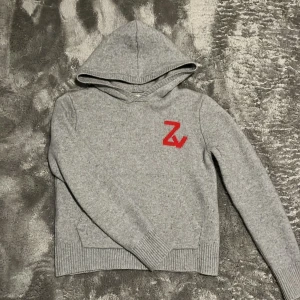 Zadig tröja - Grå stickad hoodie med röd Zv-detalj på bröstet och stor röd döskalle på ryggen.