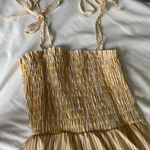 Gul och vit randig klänning med smock och knytband - Säljer en söt gul och vit randig klänning från SHEIN med smock upptill och knytbara axelband. Klänningen har en luftig passform och är perfekt för varma dagar. Längden är mittilång och materialet känns lätt och somrigt.