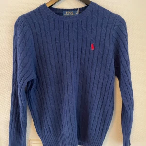 Blå tröja från Polo Ralph Lauren - Kabelstickad blå tröja från Polo Ralph Lauren som har råkat krympa vid tvätt så skulle uppskatta den att vara storlek S. Annars är tröjan bra överlag.