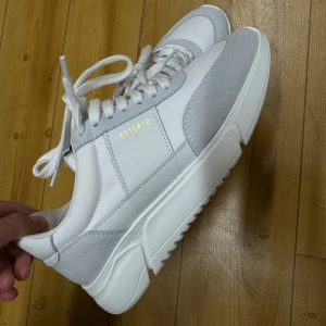 Vita och grå sneakers från Axel Arigato - Snygga sneakers i vitt och ljusgrått från Axel Arigato.  Aldrig använda då de är för små! Nypris 2700!