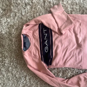 Rosa sweatshirt från GANT - Säljer en rosa sweatshirt från GANT med en mörkblå panel och vit logga framtill. Tröjan har rund halsringning och långa ärmar. Perfekt för en avslappnad och stilren look. Köpt för några år sedan men är i super skick🤍