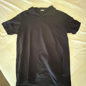 Svart piké t-shirt från Filippa K - Säljer en klassisk svart piké t-shirt från Filippa K. T-shirten har korta ärmar, krage och normal passform. Perfekt för en stilren och enkel look. Materialet känns mjukt och bekvämt.
