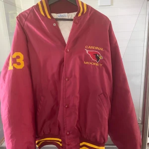 Röd varsityjacka Cardinal Mooney - Säljer en as fet röd varsityjacka med gula detaljer och broderad text 'Cardinal Mooney' samt nummer 13 på ärmen. Jackan har knappar framtill, ribbade muddar och krage med gula ränder. Perfekt för dig som gillar amerikansk high school-stil.