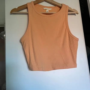 Persiko/aprikos-färgad ribbad croppad linnetopp - Säljer en persiko-aprikos-färgad croppad linnetopp med ribbad struktur. Toppen är ärmlös och har en rund halsringning. Stl M, men även väldigt stretchigt. Enbart använt fåtal gånger, så mycket bra skick. Kontakta gärna vid mer information och mer exakta mått. Säljer samma på vinted så hör gärna av er innan köp!