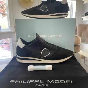 Philippe Model svarta sneakers med vita detaljer - Säljer ett par snygga svarta Philippe Model sneakers med vita detaljer och logga på hälen. Skorna har snörning, rund tå och platt sula. Kommer med originalkartong och extra skosnören. Pris kan diskuteras vid snabb affär 