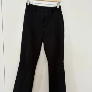 Svarta kostymbyxor med bootcut - Snygga svarta kostymbyxor med klassisk passform och bootcut-ben. Midwaist byxor. Byxorna har hällor för bälte, diskreta fickor och stängs med dragkedja och knapp framtill. Perfekta till en stilren look.