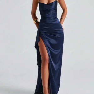Marinblå långklänning med slits - Snygg marinblå långklänning i satin med smala justerbara axelband och slits på ena sidan. Klänningen har figurnära passform och  korsade band i ryggen. Helt oanvänd, va till balen men hittade en annan så har ingen användning för den. Strl 34 (xs)