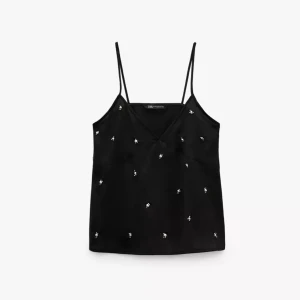 Svart linnetopp med broderade detaljer från Zara - Säljer en svart linnetopp från Zara med tunna axelband och v-ringning. Toppen har små vita broderade detaljer utspridda över hela plagget. Perfekt att styla till både jeans och kjol!