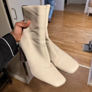Beige boots med fyrkantig tå och klack - Snygga beige boots med fyrkantig tå och klack. Skorna har en struktur som påminner om ormskinn och är tillverkade i syntetmaterial. Perfekta för dig som vill sticka ut med en trendig look.