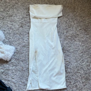 Vit axelbandslös klänning med slits - Elegant vit axelbandslös klänning med en slits på sidan. Perfekt för student. Klänningen har en figurnära passform och är tillverkad i ett mjukt material. Använd bara en gång.💖kan gå ner i pris vid snabb affär.