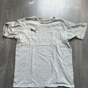 Grå t-shirt från Puma - Säljer en grå t-shirt från Puma med korta ärmar och en klassisk passform. Perfekt för en avslappnad stil eller träning. Puma-loggan är tryckt på bröstet. Skön och enkel att matcha med det mesta. 🐾