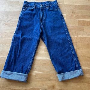 Blå jeansbyxor från Sweet SKTBS - Säljer ett par coola blå jeansbyxor från Sweet SKTBS. Byxorna har en loose passform med breda ben och uppvikta fållar. De har klassiska femficksdetaljer och ett snyggt tryck på baksidan med texten 'Sweet SKTBS'. Perfekta för en avslappnad stil!