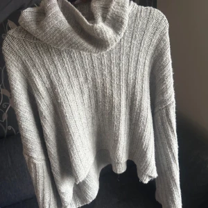 Grå stickad polotröja - Mysig grå stickad polotröja med breda ribbade ränder och oversized passform. Tröjan har lång ärm och hög polokrage, perfekt för kyliga dagar. Enkel att matcha med jeans eller kjol.