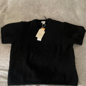 Svart kortärmad tröja från Gina Tricot Young - En svart, enkel och stilren kortärmad tröja från Gina Tricot Young. Tröjan har en klassisk rund halsringning och är gjord i ett mjukt material. Aldrig använt eftersom att den är för kort. Prislapp sitter fortfarande på 🥰