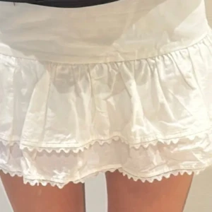 Vit volangkjol zara - Söt vit kjol med dubbla volanger och dekorativ kant nertill. Kjolen har en kort längd och är perfekt för varma dagar. Tillverkad i ett lätt och luftigt material som ger en avslappnad känsla.