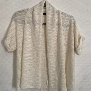 Vit stickad kofta från Rut & Circle - Säljer en vit stickad kofta från Rut & Circle. Den har en öppen design med korta ärmar och ett luftigt stickat material. Perfekt för lager-på-lager-stil. Passar till både vardag och mer uppklädda tillfällen.