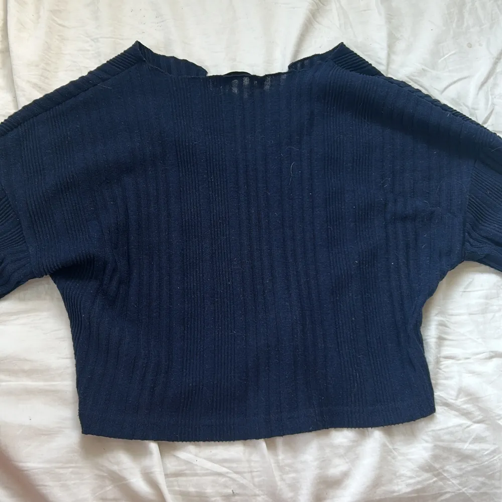 Säljer en mörkblå croppad tröja från NA-KD med ribbad struktur. Tröjan har långa ärmar och en liten v-ringning vid halsen. Perfekt till jeans eller kjol för en avslappnad look.. Neuletakit & Villapaidat.
