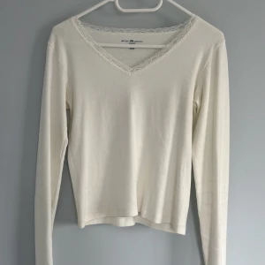 Vit långärmad topp med spets från Brandy Melville - Säljer en vit långärmad topp från Brandy Melville med v-ringning och fina spetsdetaljer längs halsringningen. Använt den endast en gång och skulle säga den är en xs-s